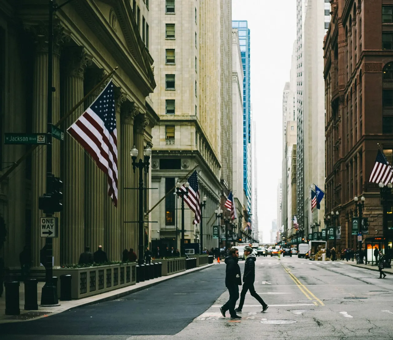 LaSalle Street at Jackson Boulevard in the Chicago Loop by day, with flags on stone office buildings and people crossing the street.
