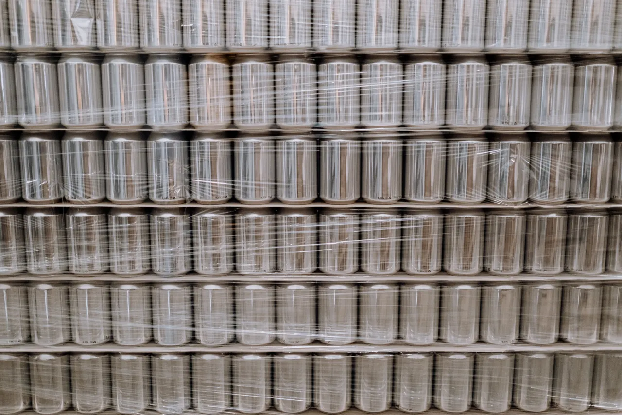 Pallets of beverage cans stacked in rows and wrapped in clear film.