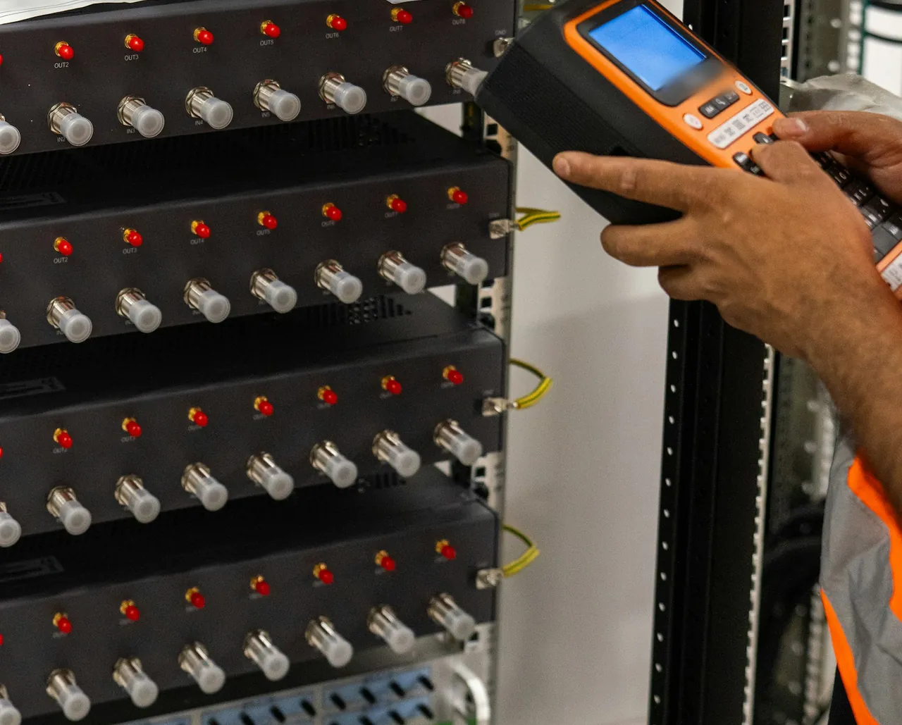 A technician's hands hold a label printer beside a rack of network equipment, labeling its ports.