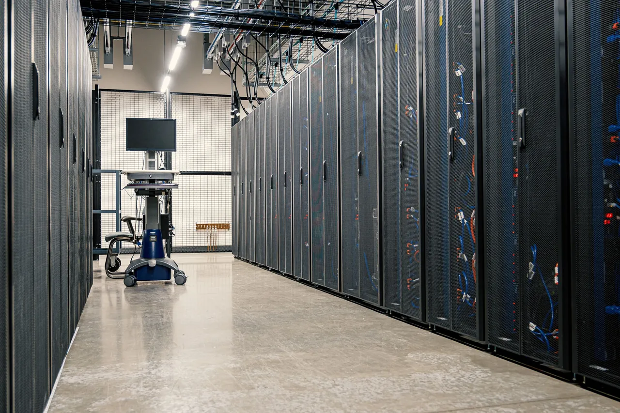 A data center aisle between rows of mesh-door server racks under overhead cable trays, with a crash cart at the far end.