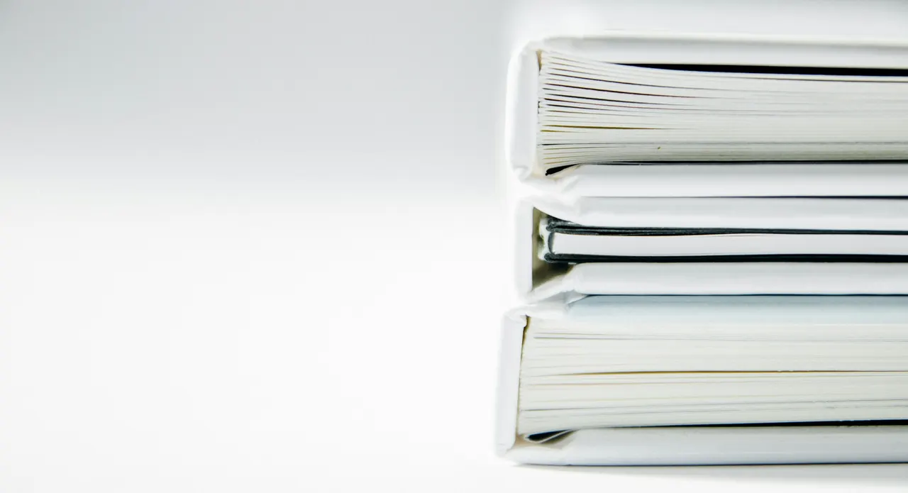 A stack of thick white binders of printed statements, seen side on against a white wall.