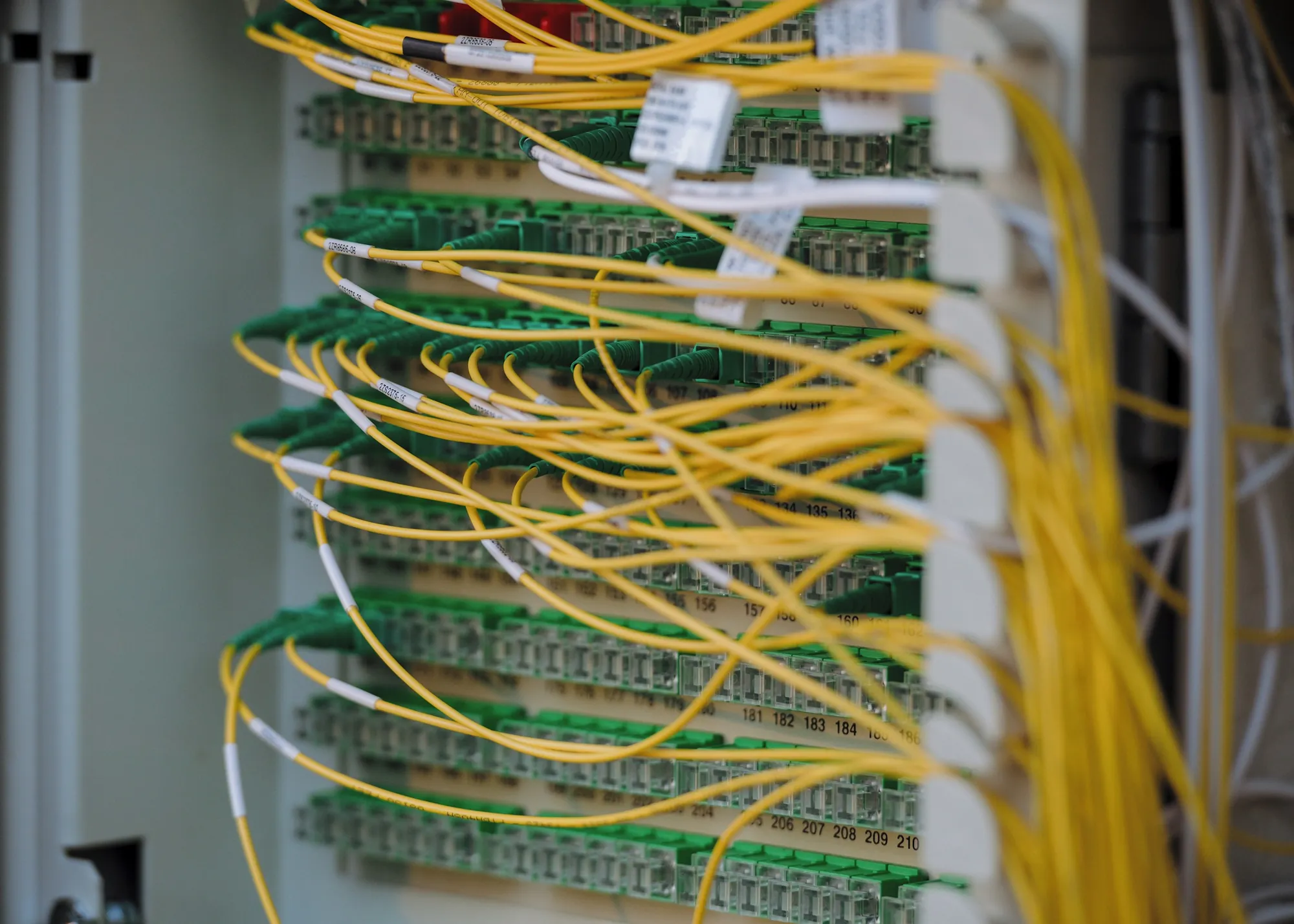 A fiber distribution frame in a telecom cabinet: yellow single-mode jumpers plugged into rows of green adapters, each port numbered and each jumper labeled.