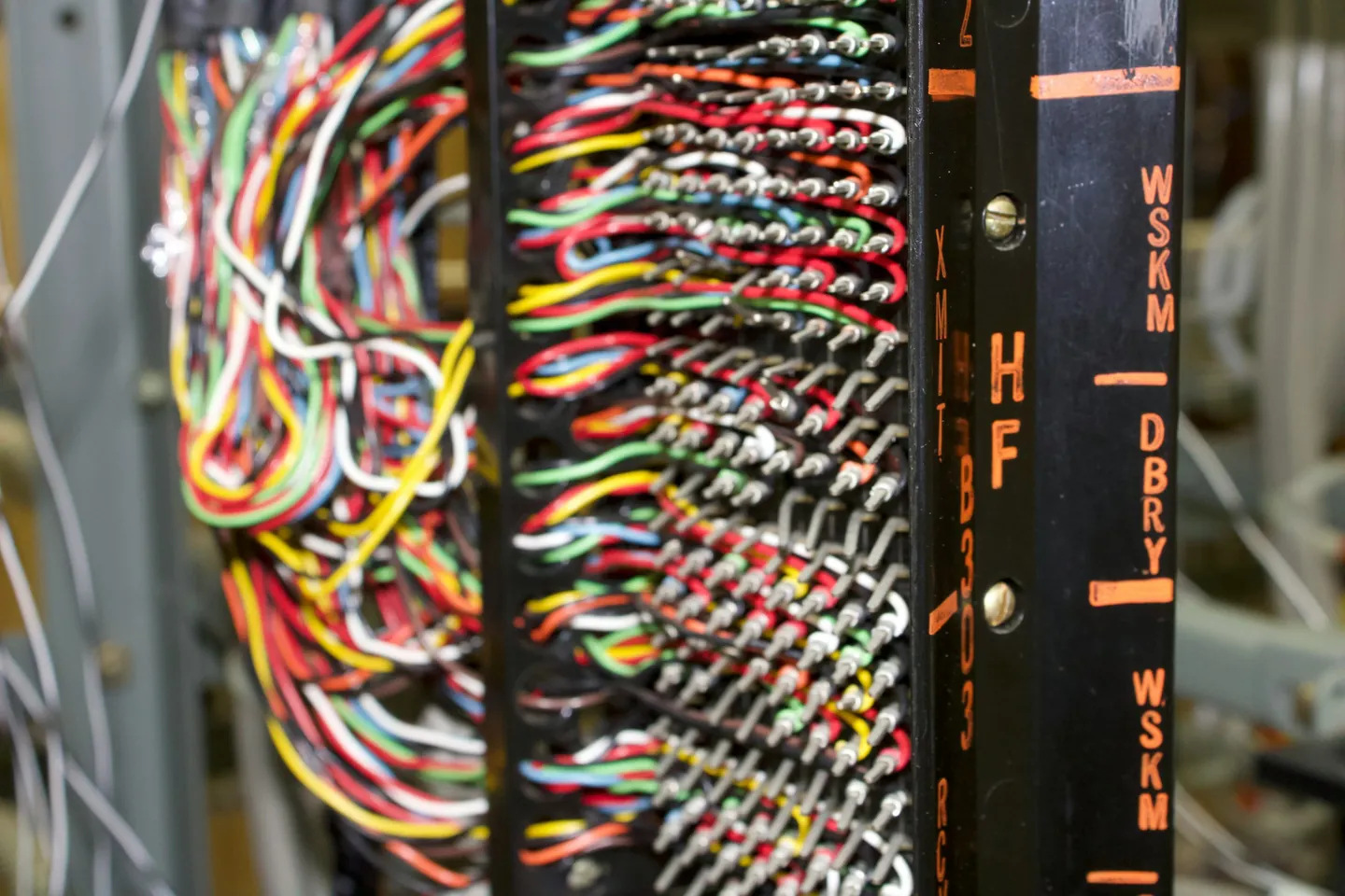 A telephone cross-connect frame with hundreds of colored copper pairs punched down in rows beside stenciled circuit labels.